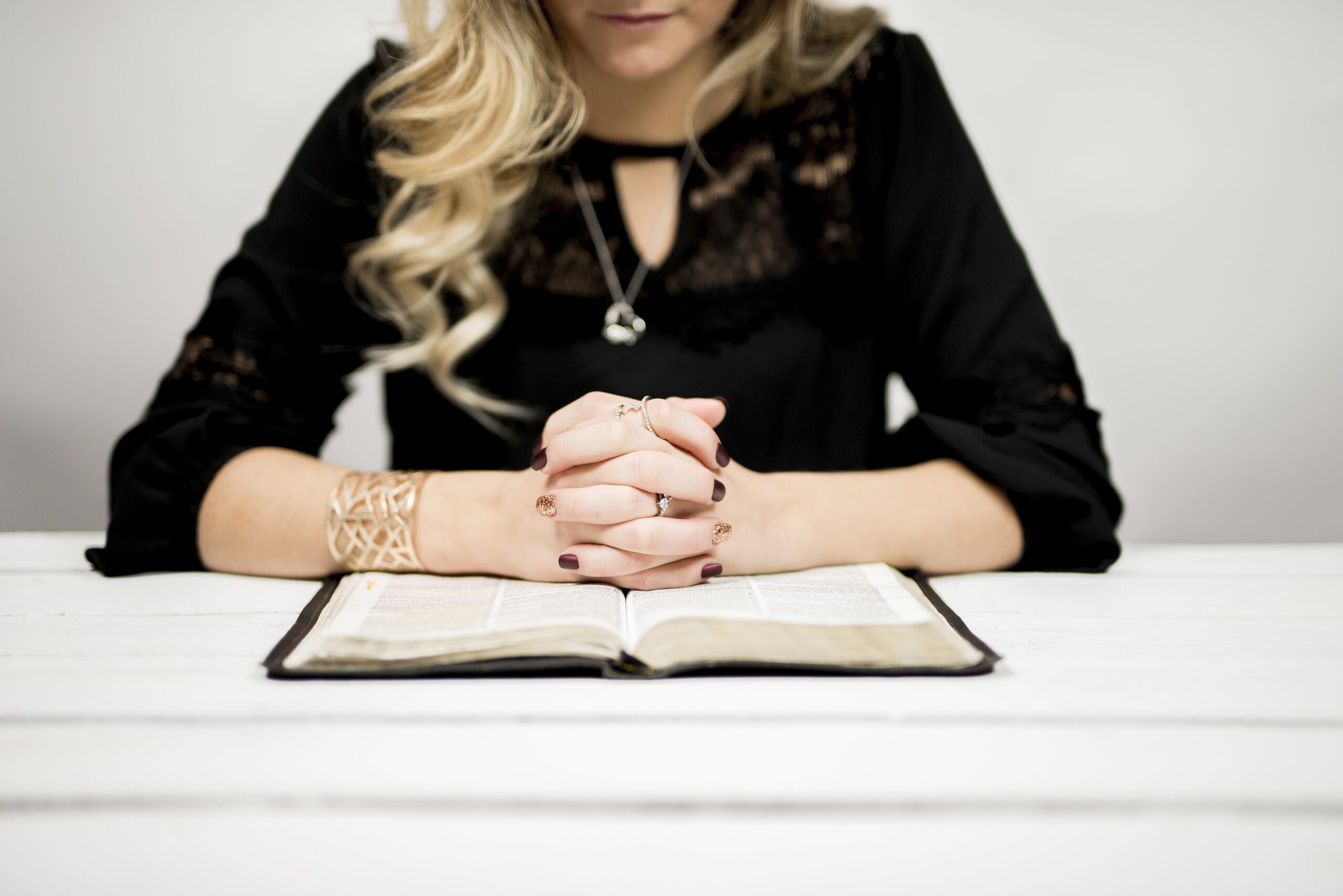 A blonde woman reading a bible on the table against a white background