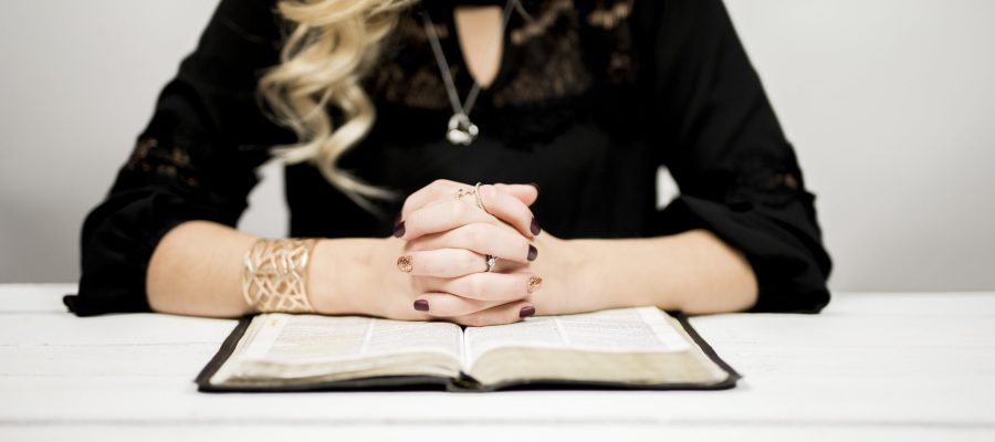 A blonde woman reading a bible on the table against a white background